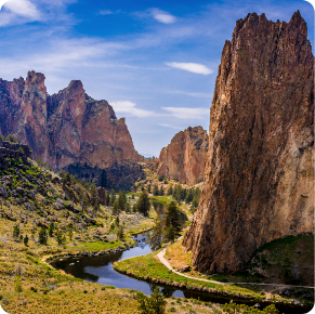 A winding river flows through a lush valley surrounded by towering rock formations. The sky above is clear with a few scattered clouds, and dense greenery covers the landscape at the base of the rock cliffs. The exterior scene is tranquil and picturesque, reminiscent of serene commercial painting services.