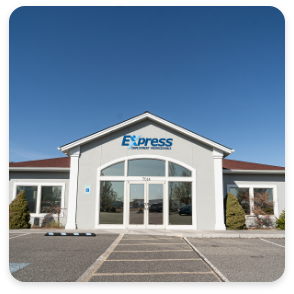 A one-story building with a peaked roof and large glass double doors at the entrance. The building has a sign that reads "Express Employment Professionals" above the doors. The exterior, recently updated by commercial painting services, is light gray with a red-brown roof. There are small shrubs and a concrete walkway.