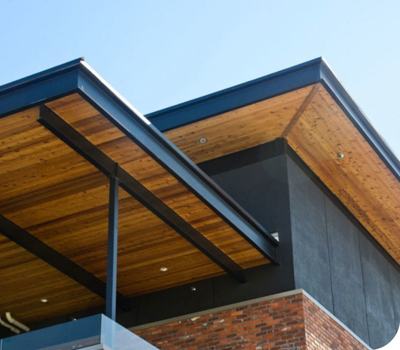 A modern building with a striking combination of materials, featuring a brick facade on the lower portion, black walls above, and a flat, overhanging wooden roof with black beams. The clear blue sky enhances the contemporary architectural design. Ideal for commercial painting services, its exterior impresses at every glance.