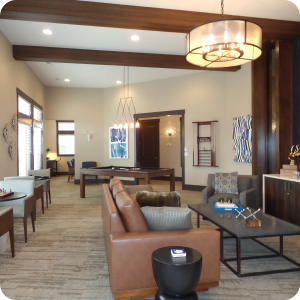 A modern living room with a beige carpet and cream-colored walls, featuring a brown leather sofa and a gray armchair. A dark wood coffee table and matching side table complement the interior, which also includes a dining area with several chairs and tables. Ideal for those seeking quality commercial painting services.